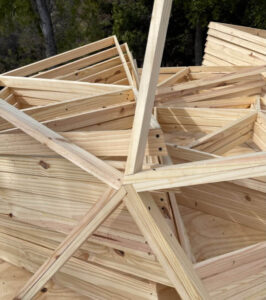 Triángulo de madera ensamblado sobre plataforma, sujeto con prensa metálica durante el montaje del domo geodésico
